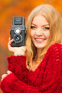时尚金发女孩年轻青摄影师在秋季公园行走用旧相机拍照橙叶背景图片