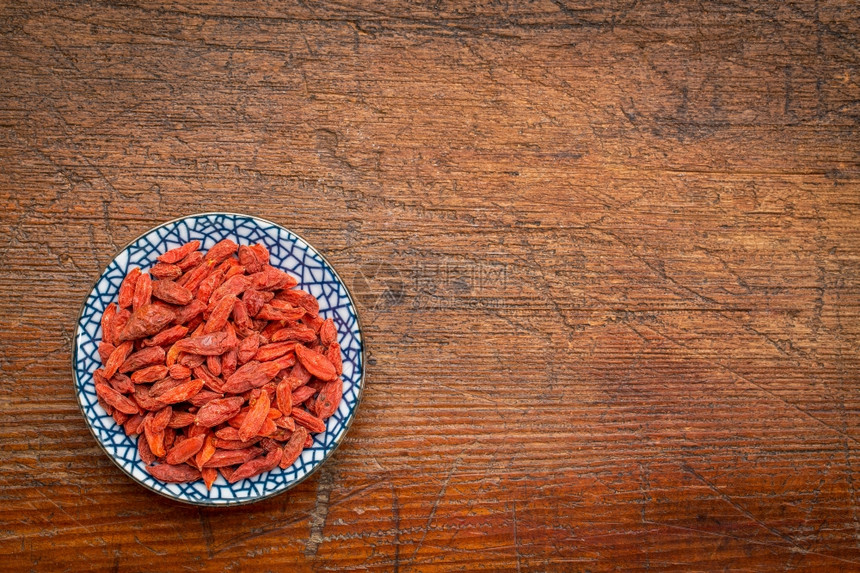 Goji浆果狼莓带复制空间的生锈木上小瓷碗图片