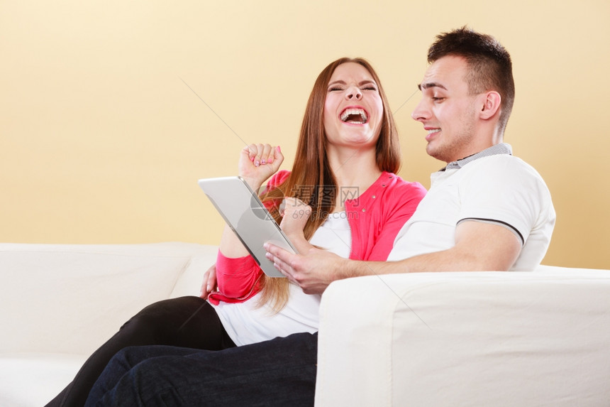 拥有电脑平板的年轻夫妇坐在家庭网上浏览的沙发图片