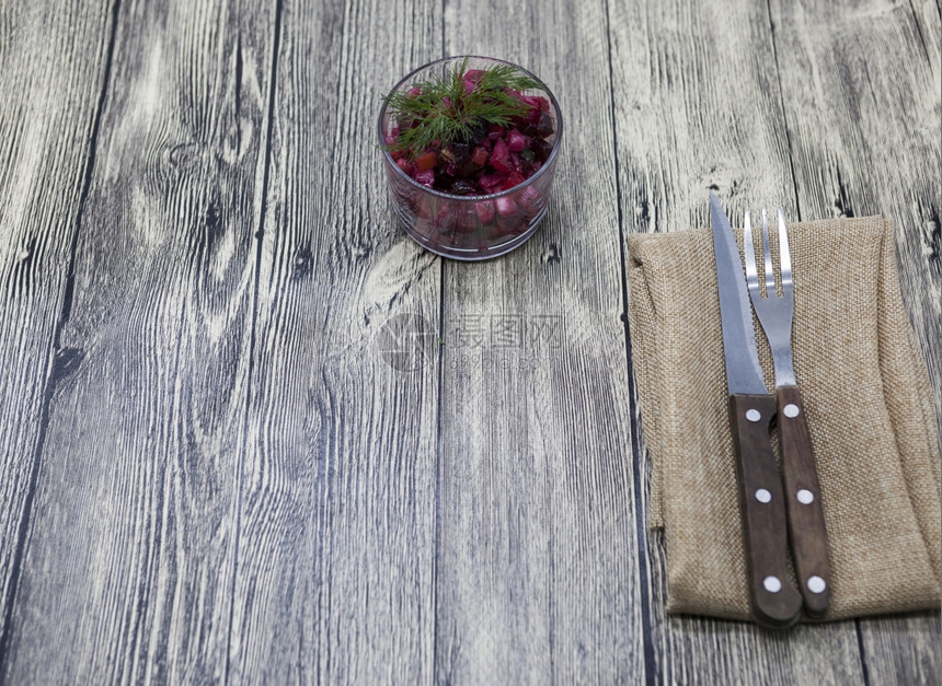 甜菜沙拉放在玻璃花瓶中用叉子和刀在木背景上图片