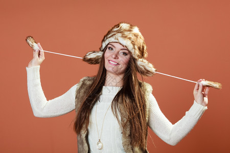 冬天时快乐的年轻女穿着时的冬季服装橙色背景的毛帽图片