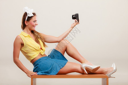 穿着发带弓裙子和高跟鞋的笑得要命的女孩用相机拍自照片图片