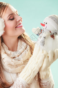 与小雪人一起微笑的可爱女人冬季带着小雪人微笑的可爱女穿着耳巾和围的迷人女孩绿色工作室冬季时尚图片