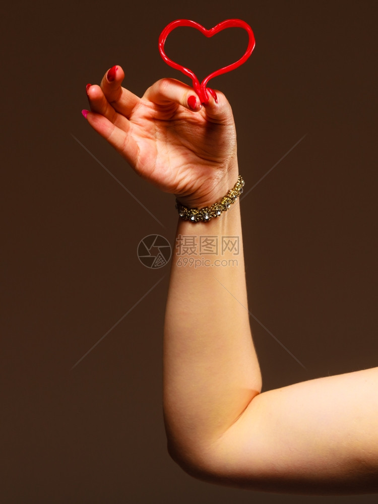 情人节39日概念棕色背景上握着红糖果心脏符号的女手摄影棚拍图片