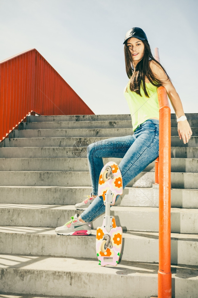 酷的长发女孩滑板坐在城市栏杆上活跃的生方式在夏天很怪异图片