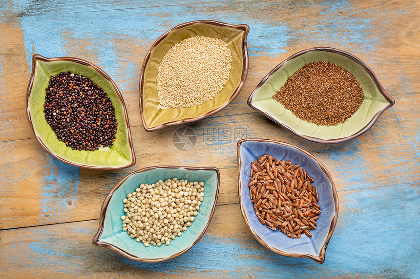 一套五种无谷质高梁塔夫阿玛兰特棕米和quinoa的免费谷类高梁棕米和quinoa顶层的叶状碗与土豆油漆的木头相对图片