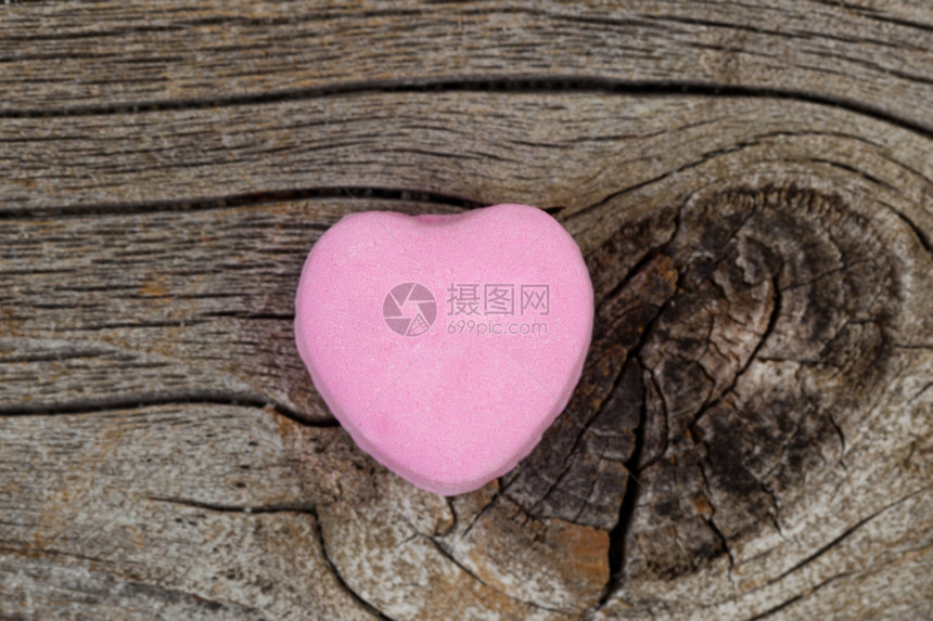 紧贴着一个粉红色的心形糖果在生锈的木头上情人节的概念图片