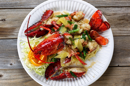 新鲜煮熟的缅因州龙虾覆盖着草药洋葱白色盘子上的酱汁图片