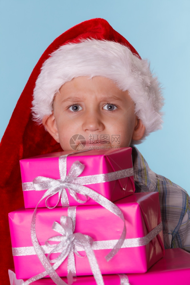 童年快乐圣诞节假期时间戴着红圣塔帮手帽子的小男孩拿着一堆粉红礼物蓝色的盒图片