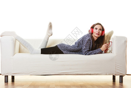 妇女随便的红色大耳机听音乐mp3坐在沙发上家里放松图片