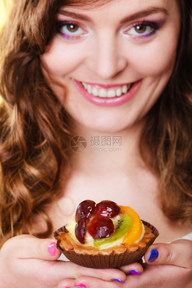 甜食面包和人的概念笑的可爱卷发女郎手持黄背景的水果蛋糕图片