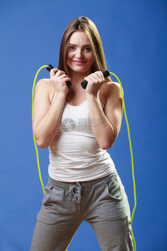 穿着运动服的美丽快乐女孩在蓝背景上跳绳图片