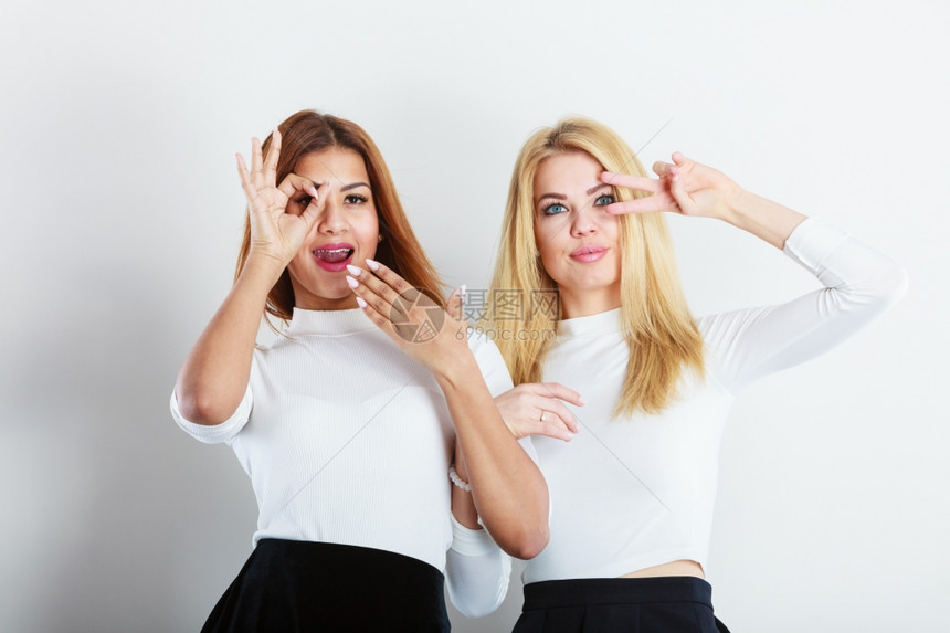 两个金发女孩和混杂种族朋友站在一起年轻时装女玩得开心手举展示标志图片