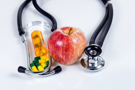 红苹果药囊和听诊器在白桌上反射良好的保健概念图片