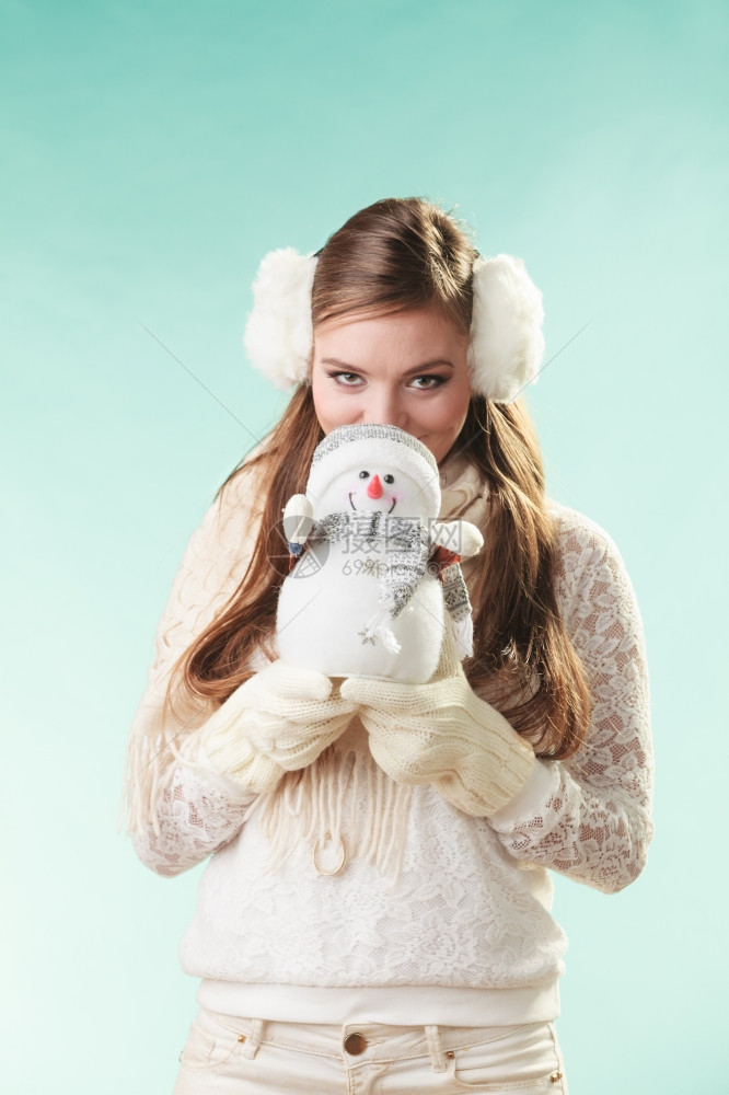 小雪人可爱的女冬季时装穿着小雪人的可爱女穿着耳罩和白色毛衣的迷人女孩在绿色工作室穿图片