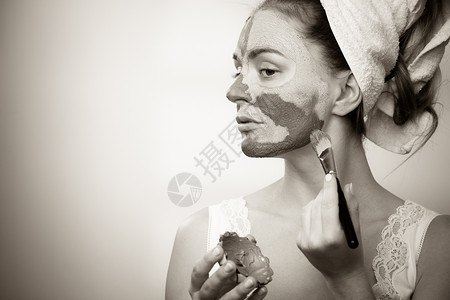 皮肤护理妇女用刷泥面罩套住脸部女孩照顾油色的皮肤美容治疗黑色白色照片背景