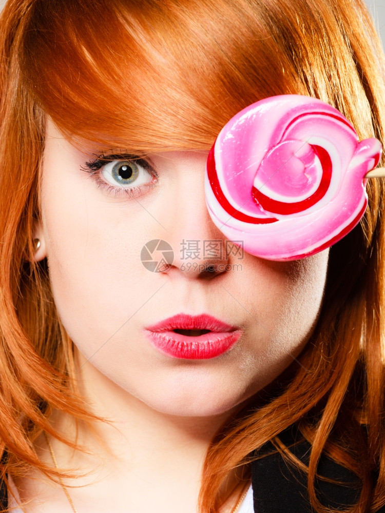 穿着糖果的红发女孩带着粉红色棒糖玩得开心遮住她的眼睛图片