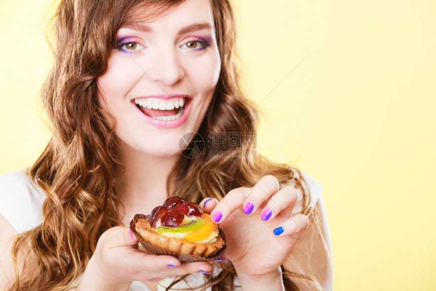 甜食面包和人的概念笑的可爱卷发女郎手持黄背景的水果蛋糕图片