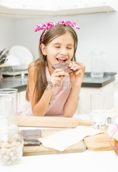 笑的可爱女孩在厨房里咬巧克力棒的肖像图片