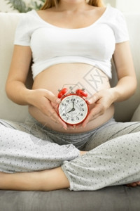 年轻孕妇在沙发上装着红色闹钟图片