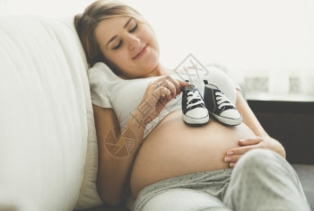 身躺在沙发上并穿着婴儿靴子的幸福孕妇照片图片