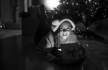 坐在壁炉旁边的地板上躺在圣诞礼物盒里的可爱笑女孩的黑白画像图片