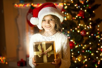 美丽的笑女孩肖像带着闪亮的礼物盒站在圣诞树上图片