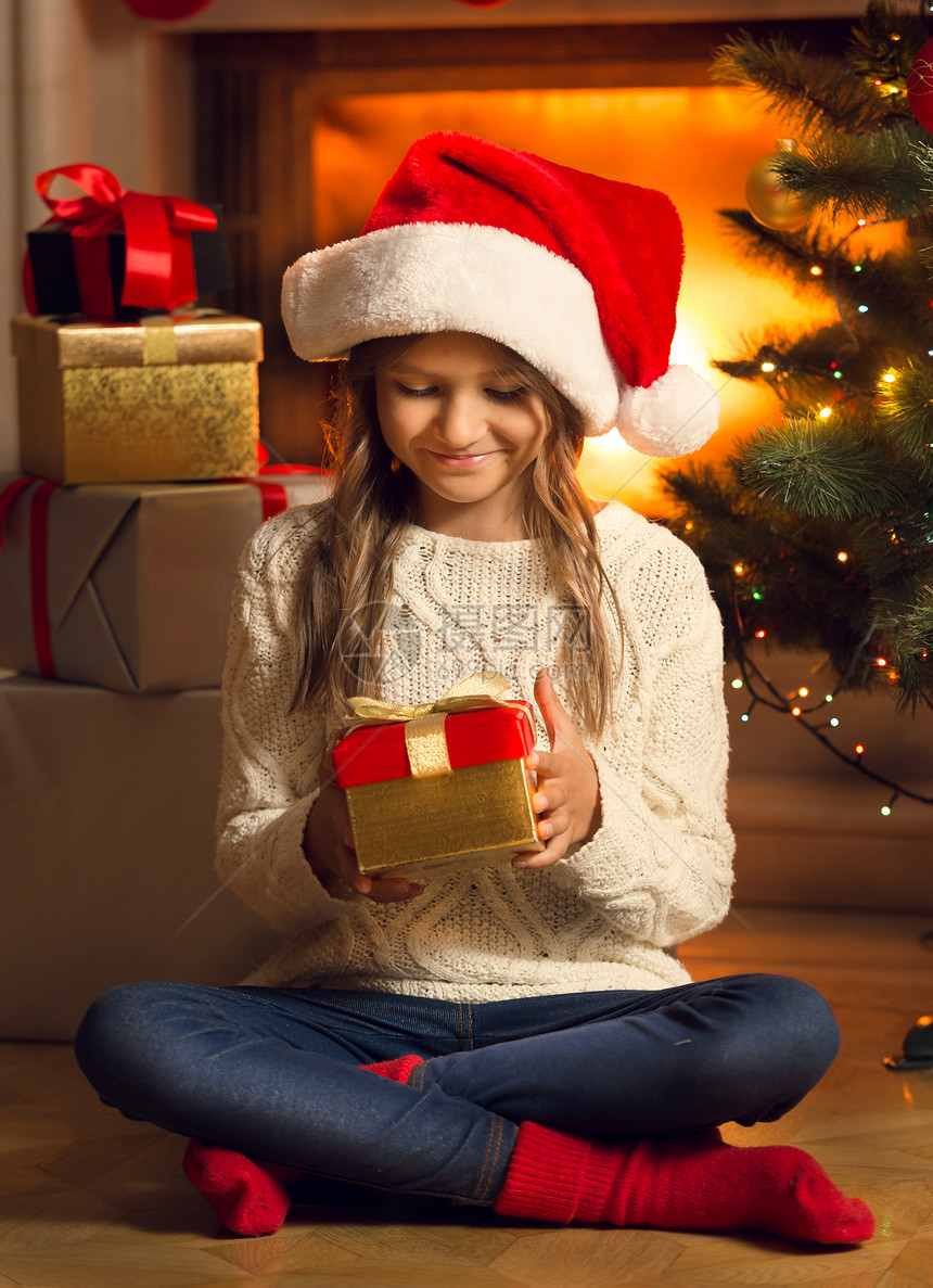 坐在地板上看着圣诞礼物的笑女孩图片
