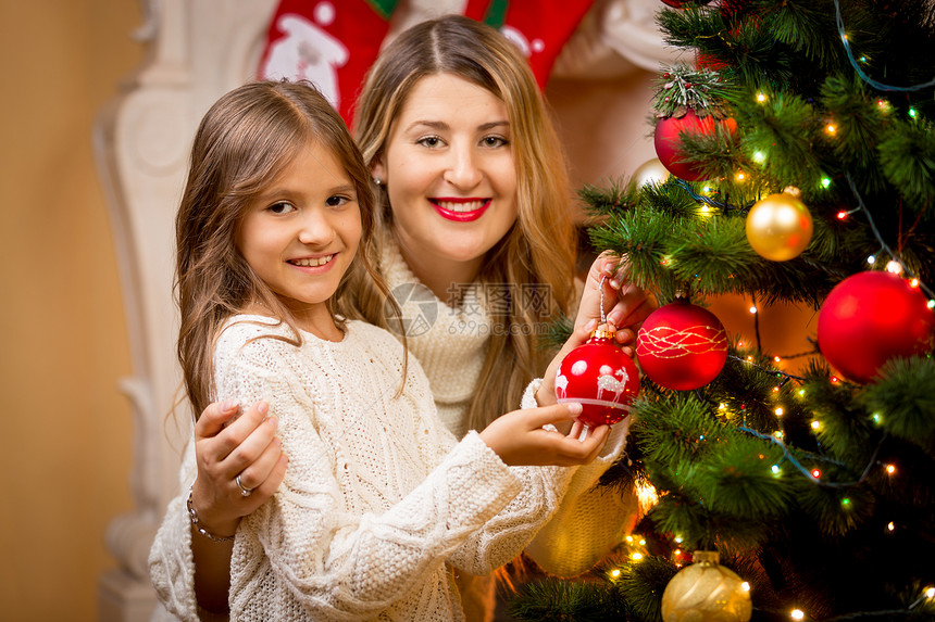 母亲和女儿在圣诞树上装饰的紧贴画像图片