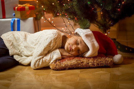 圣诞老人帽子可爱女孩的肖像睡在圣诞树下图片