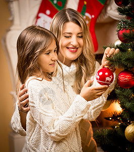 帮助母亲装饰圣诞树的微笑女孩肖像图片