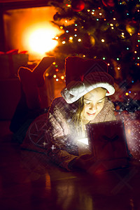 坐在圣诞树下看着闪发光的礼物盒可爱女孩肖像图片