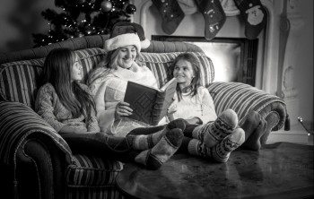 母亲与两个女儿在壁炉沙发上读书的黑白母亲肖像图片
