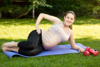快乐的孕妇在公园健身席上运动图片