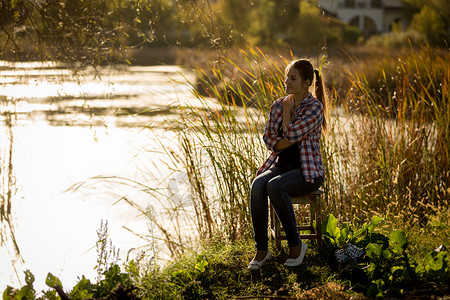 年轻女子坐在湖边日落时高清图片
