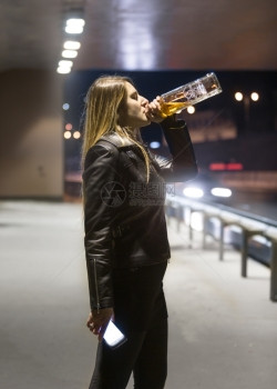 年轻女子的肖像从酒瓶和夜里喝威士忌图片