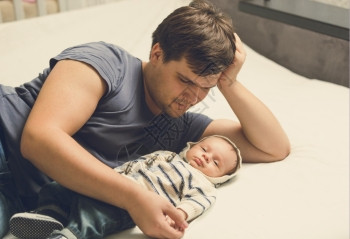 快乐的父亲和婴儿男孩躺在床上图片
