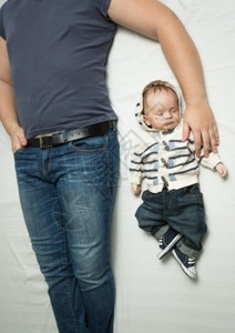 穿着牛仔裤躺在床上的年轻时尚父亲和婴儿男孩最美景照片图片