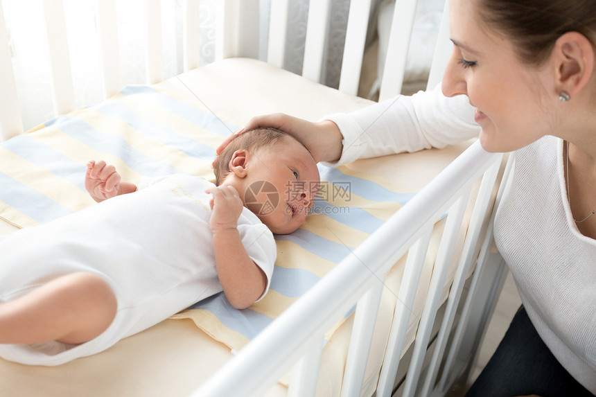 快乐的笑母亲抚摸躺在床上的婴儿肖像图片