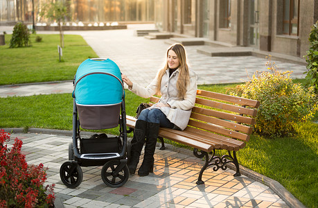美丽的母亲坐在公园长椅上摇着婴儿车图片