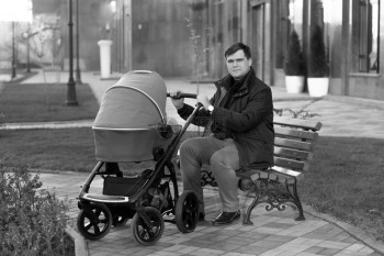 年青父亲坐在公园的长凳上带着婴儿车图片