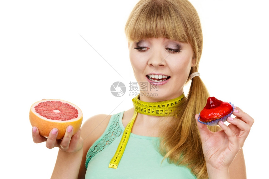 配有测量胶带的妇女握在手上蛋糕和葡萄精的选择中在甜食或新鲜水果之间作出决定饮食选择图片