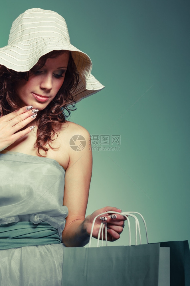 穿着礼服戴帽子的女人拿着购物袋时髦的年轻女人喜欢商店新衣服穿着绿色轻礼服的女孩高兴帽子拿着购物袋图片