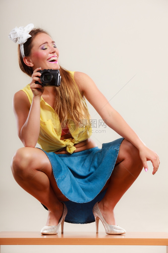 穿着发带弓裙子和高跟鞋的笑得开心女孩用照相机拍图片