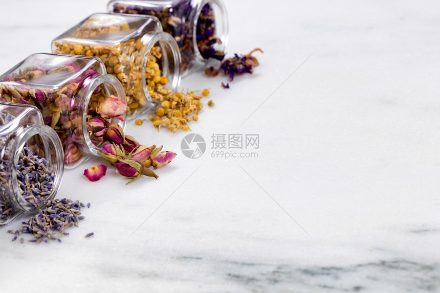 玻璃罐中洒到白大理石上的草药和香料前视线选择地聚焦于第二个有玫瑰花蕾的罐子上图片