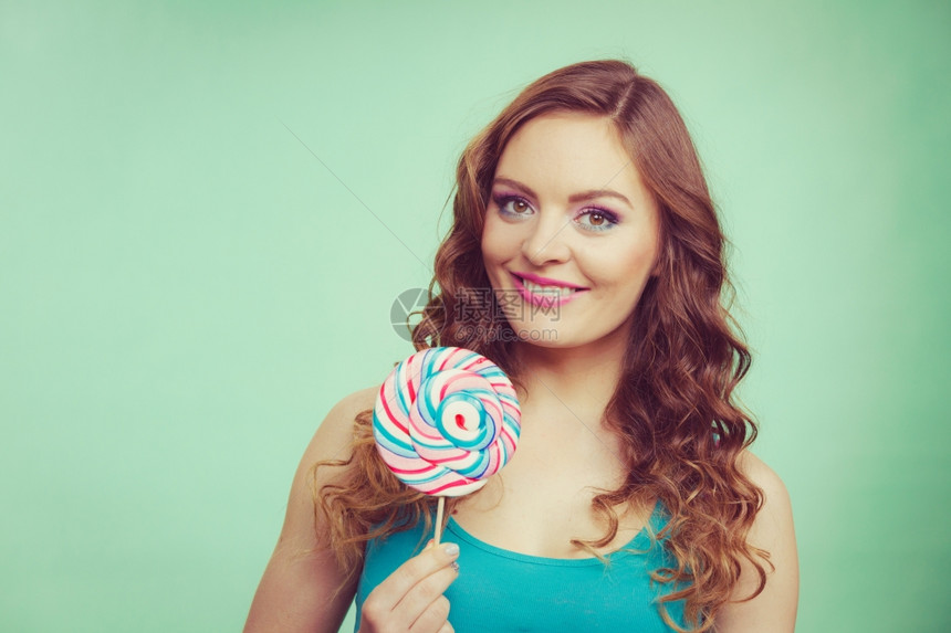 迷人的有魅力女子快乐孩手拿着多彩的棒糖甜食和享受的概念工作室拍摄绿色蓝背景刻画图像图片