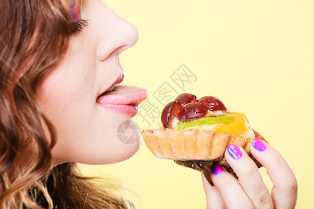甜和快乐的概念可爱的女人吃水果蛋糕玩得开心的舌头脸部形象黄色背景图片
