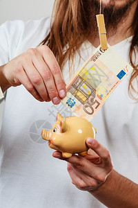 男人用钞票和小猪银行的手花钱概念男人用小猪银行和欧元钞票现金的手储蓄图片