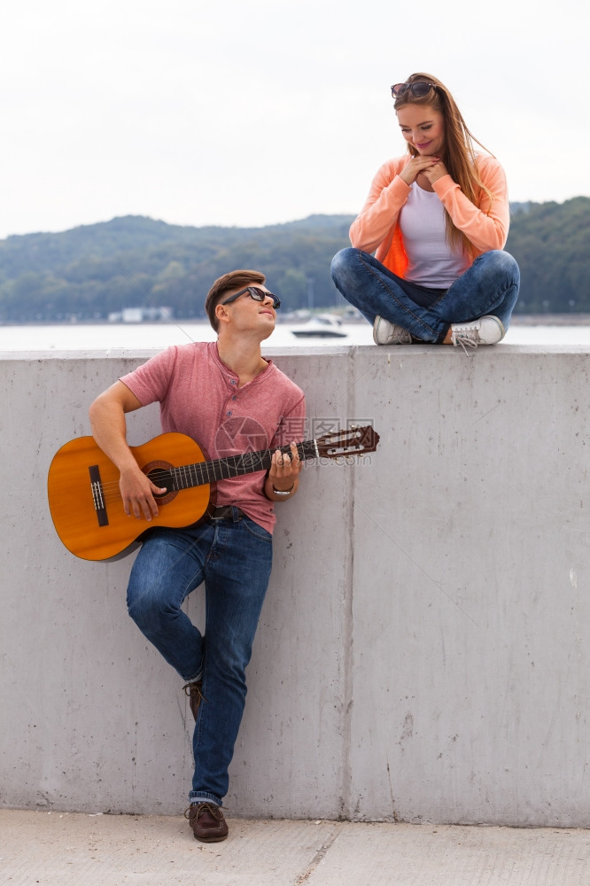 爱浪漫关系音乐概念快情侣在海岸度过时间年轻男孩在给女弹吉他图片