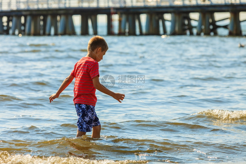 男孩在沙滩上行走外面有水的乐趣和欢男孩在海中行走孤独的孩子穿着夏衣在户外玩耍图片